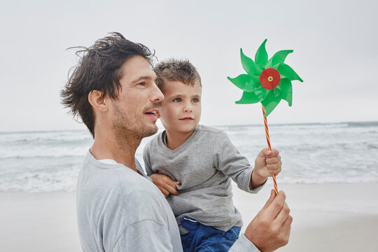 Father carrying son on the beach holding green pinwheel