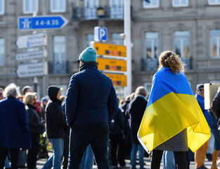 Rear view of woman wearing Ukrainian flag walking on street at protest in front of Russian Consulate solidarity Ukrainians against the war after Russian invasion - obrazy, fototapety, plakaty