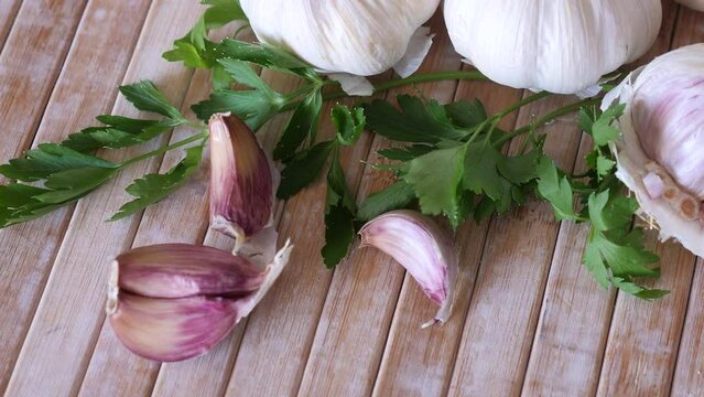 Unpeeled spicy garlic cloves and sprigs of fresh aromatic parsley on wooden cutting board. Cooking ingredients. Traditional condiments 