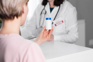 A woman holds a white jar of medicine, a doctor is in the background