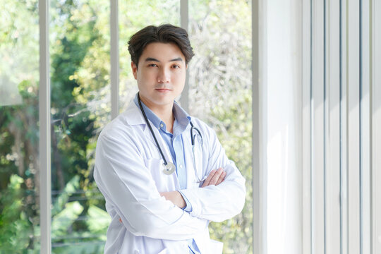 Portrait Of Asian Young Doctor Standing, Cross Arms Posing Near Windows In Medical Office. Ratio 16:9