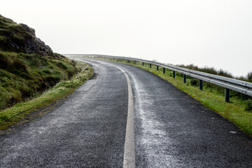 Small narrow asphalt road with bends in a mountains and fog in the background. Dangerous conditions in country side. West of Ireland.