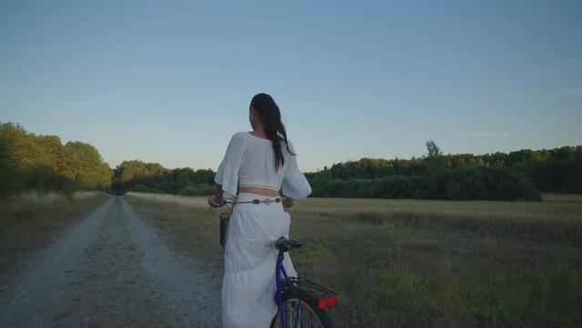 Italian Latin woman in white dress during sunset in Sweden one hot summer evening enjoying her bike ride in the while next to barley fields. 
