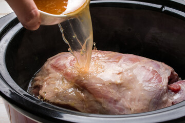Crop person pouring broth in slow cooker with raw meat