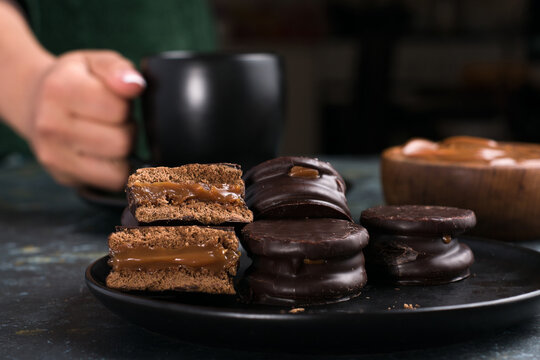 Alfajores with dulce de leche against person holding cup