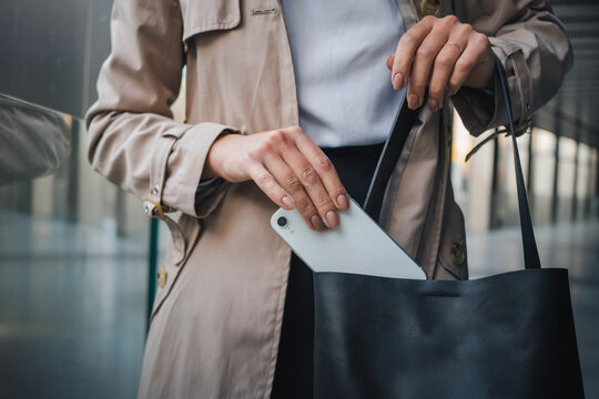 Unrecognizable woman putting smartphone into handbag