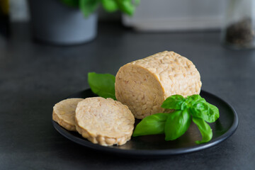 Raw Tempeh or Tempe, made of fermented soybean seeds on kitchen table. Tempeh Slices on plate with herbs. Soya protein. Plant based meat concept. Healthy eating. Go vegan. Selective focus, copy space