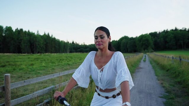 Italian Latin woman in white dress 120 fps during sunset in Sweden one hot summer evening enjoying her bike ride in the while next to barley fields. 