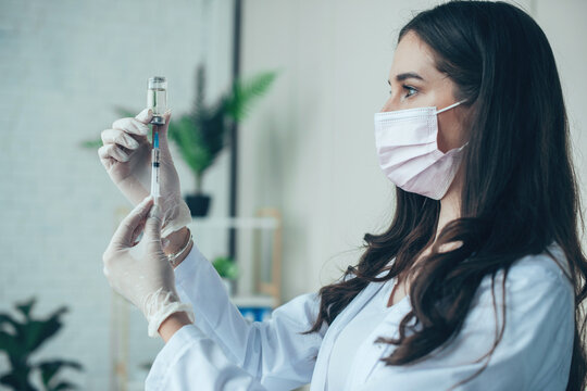 Doctor with medical mask and gloves preparing a vaccine in syringe for injecting the patient at hospital. Doctor or nurse with syringe preparing for injection