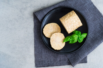 Top view raw Tempeh or Tempeh, made of fermented soybean seeds. Tempeh Slices on plate with herbs. Soya protein. Plant based meat concept. Healthy Cooking and eating. Go vegan. Flat Lay, copy space