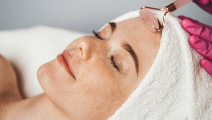 Woman receiving face massage with jade stone roller at spa salon. Beauty woman face skin care. Facial beauty. Natural beauty.