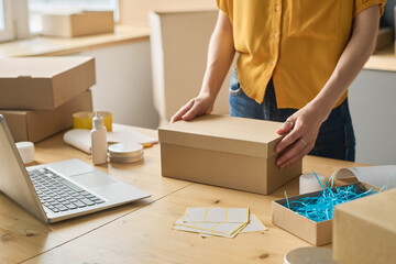 Close-up of warehouse worker packing online orders in cardboard boxes at table before shipping