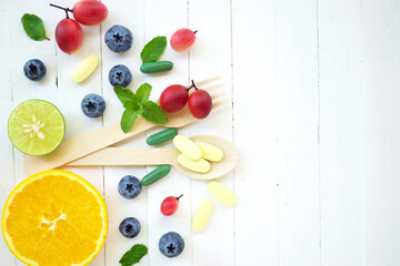 Naklejka na ściany i meble Multivitamins and supplements on wooden spoon with orange, lime and blueberry on white wooden background.