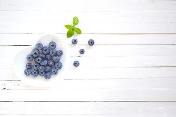 Top view blue berry on white heart shape plate on plank white wood background.