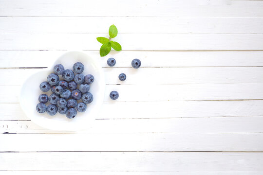 Top View Blue Berry On White Heart Shape Plate On Plank White Wood Background.