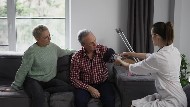 Woman therapist measuring blood pressure of senior man at home