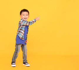 happy asian kid standing  and pointing over yellow background