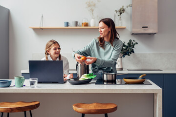 Woman cooks a meal with her curious schoolgirl daughter nearby