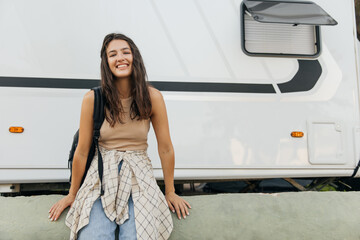 Happy caucasian young lady smiling broadly looking at camera standing by van with house. Brunette...