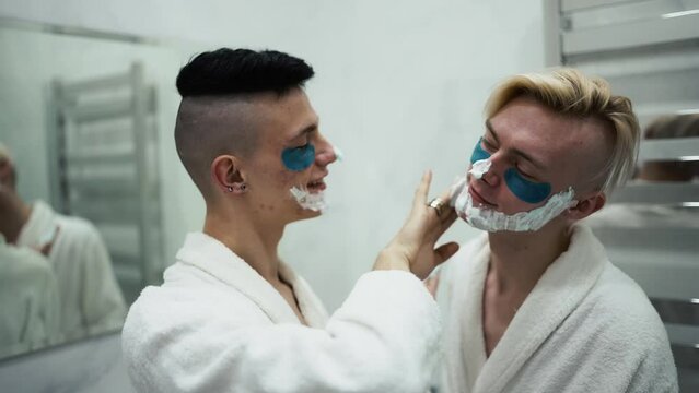Male couple having fun, applying shaving foam doing morning routine together in bathroom