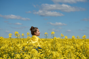 Fototapeta premium natural Ukrainian flag, girl on a yellow-blue background, woman wrapped in a Ukrainian flag against a background of a yellow field and a blue sky