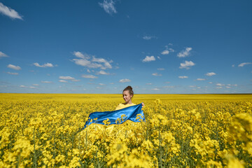 Fototapeta premium woman with the Ukrainian flag, waving ukrainian flag, woman with a flag of Ukraine in a yellow rapeseed field