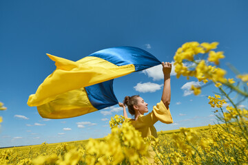 woman with the Ukrainian flag, waving ukrainian flag, woman with a flag of Ukraine in a yellow rapeseed field