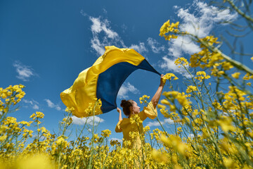 woman with the Ukrainian flag, waving ukrainian flag, woman with a flag of Ukraine in a yellow rapeseed field - obrazy, fototapety, plakaty