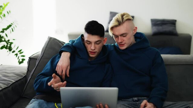 Loving gay couple spend time at home, watching movie togather on laptop