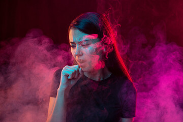 Smoker's cough. Sick young man with stressed emotions isolated over dark pink background with clouds of smoke in neon. Concept of health, addiction
