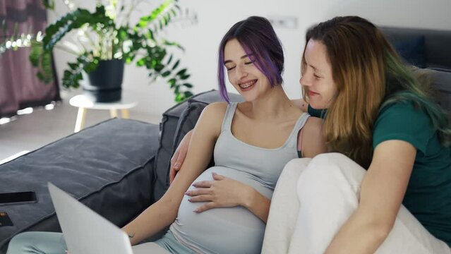 Happy gay pregnant woman using laptop computer with her wife on sofa, slow motion