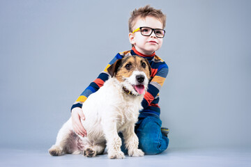 Happy boy in glasses with a dog on a light background in the studio