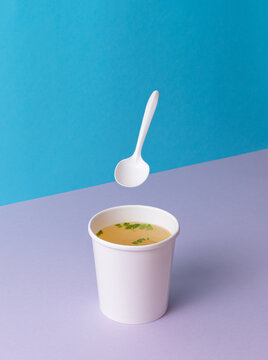 A Chicken broth soup in takeaway cup vith levitation spoon. Minimalistic Blue and purple background with copy space