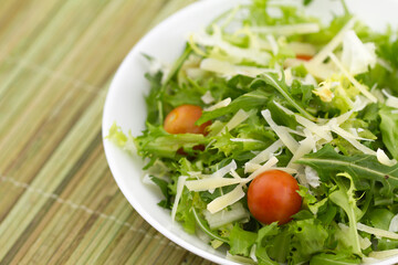 Fresh green salad: parmesan cheese, cherry, lettuce, oil on bamboo background