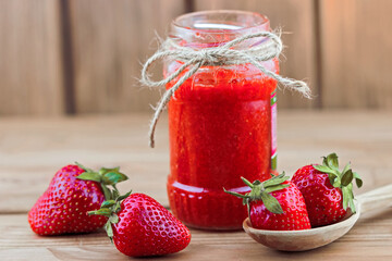 Jar of strawberry mash with fresh strawberries in the spoon on wooden background