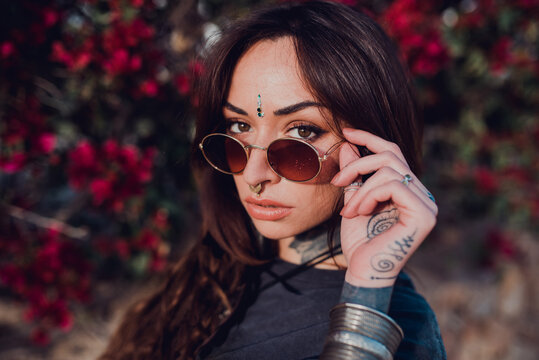 Woman in sunglasses against bush with colorful flowers in park