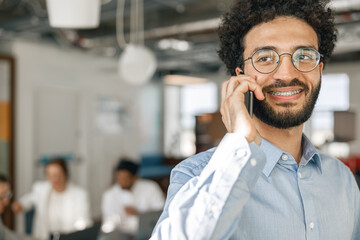 Smiling businessman talking phone standing in office on colleagues background