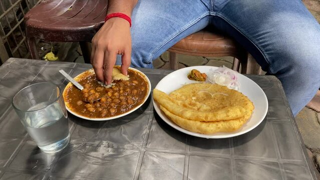 Man eating Puri with Chole after breaking it. It's an Indian breakfast dish called Chole Bhature, sometimes referred to as poori. It's a delicious dish made in India