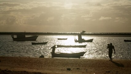 Silhouette of two men preparing a small rowing boat to go fishing with a fishing cast net at a small bay full of anchored boats in the golden hour - Powered by Adobe