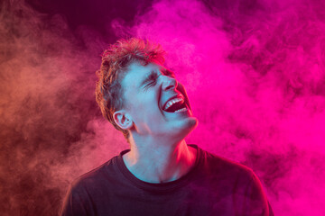 Despair. Shouting excited young man with bright emotions isolated over pink background with smoke. Concept of mental health, art, human emotions