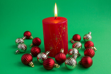 Christmas composition with red burning candle and colored beans on the green background. Closeup.