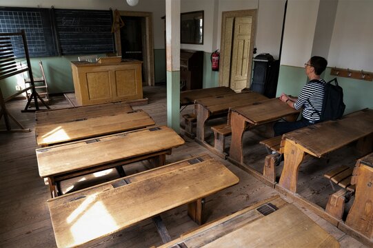Als Erwachsener zu Besuch in einem historischen Klassenraum auf sehr engen und unbequemen Schulb&auml;nken