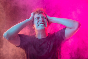 Emotional pain. Young man in deep emotional shock isolated over pink background with clouds of smoke. Concept of mental health, art, emotions