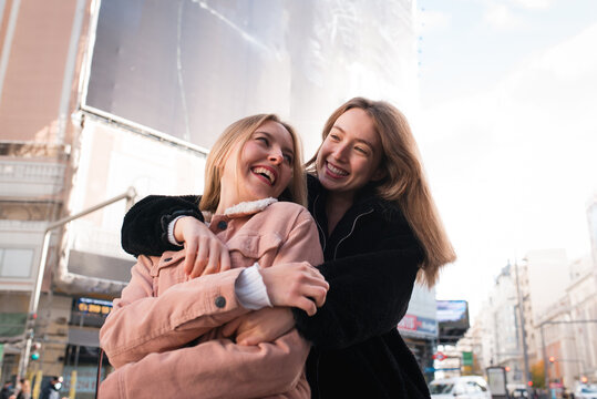 Happy women hugging on street during city stroll