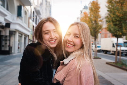 Smiling female friends looking at camera in city
