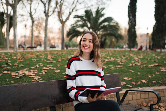 Happy young woman with book resting in park