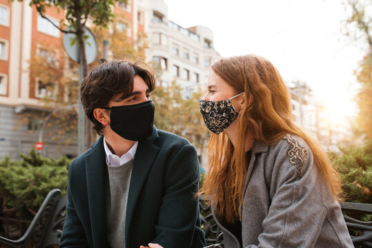 Young couple in masks resting on bench