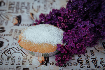 a baked cupcake next to a bouquet of lilacs 