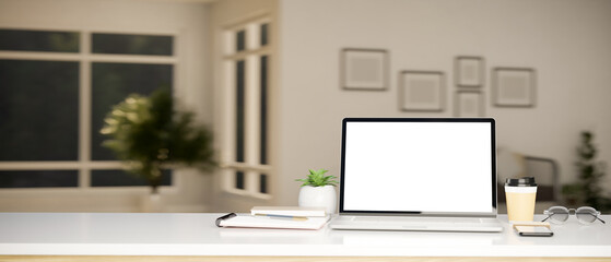 Modern working tabletop with laptop mockup and copy space over blurred living room in background.