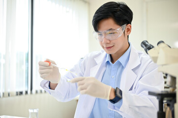 Smart Asian male scientist concentrating adjusts a virus sample in a Petri dish in his lab.